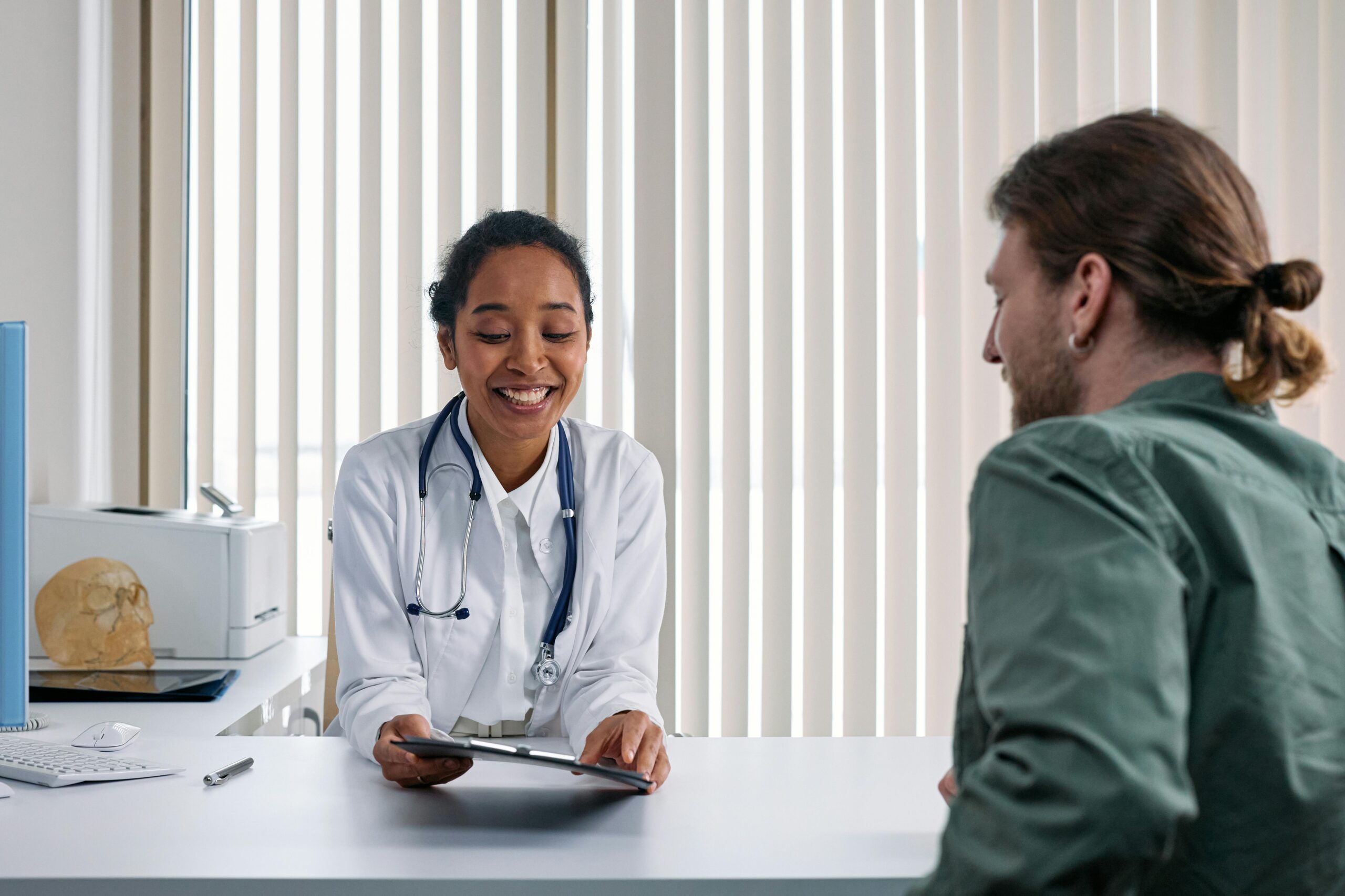 a smiling female doctor at a desk explaining or talking to a young male patient